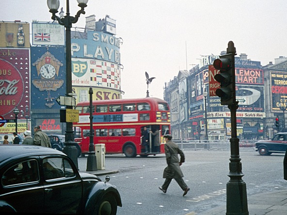 A car, pedestrian crossing the road, red London bus and advertising billboards in London's Piccadilly Circus in the 1960s